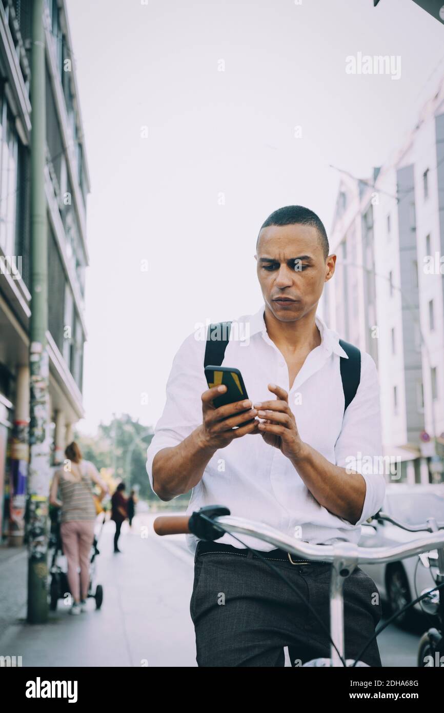 Uomo d'affari che usa il telefono cellulare mentre si guida in bicicletta sul marciapiede dentro città Foto Stock