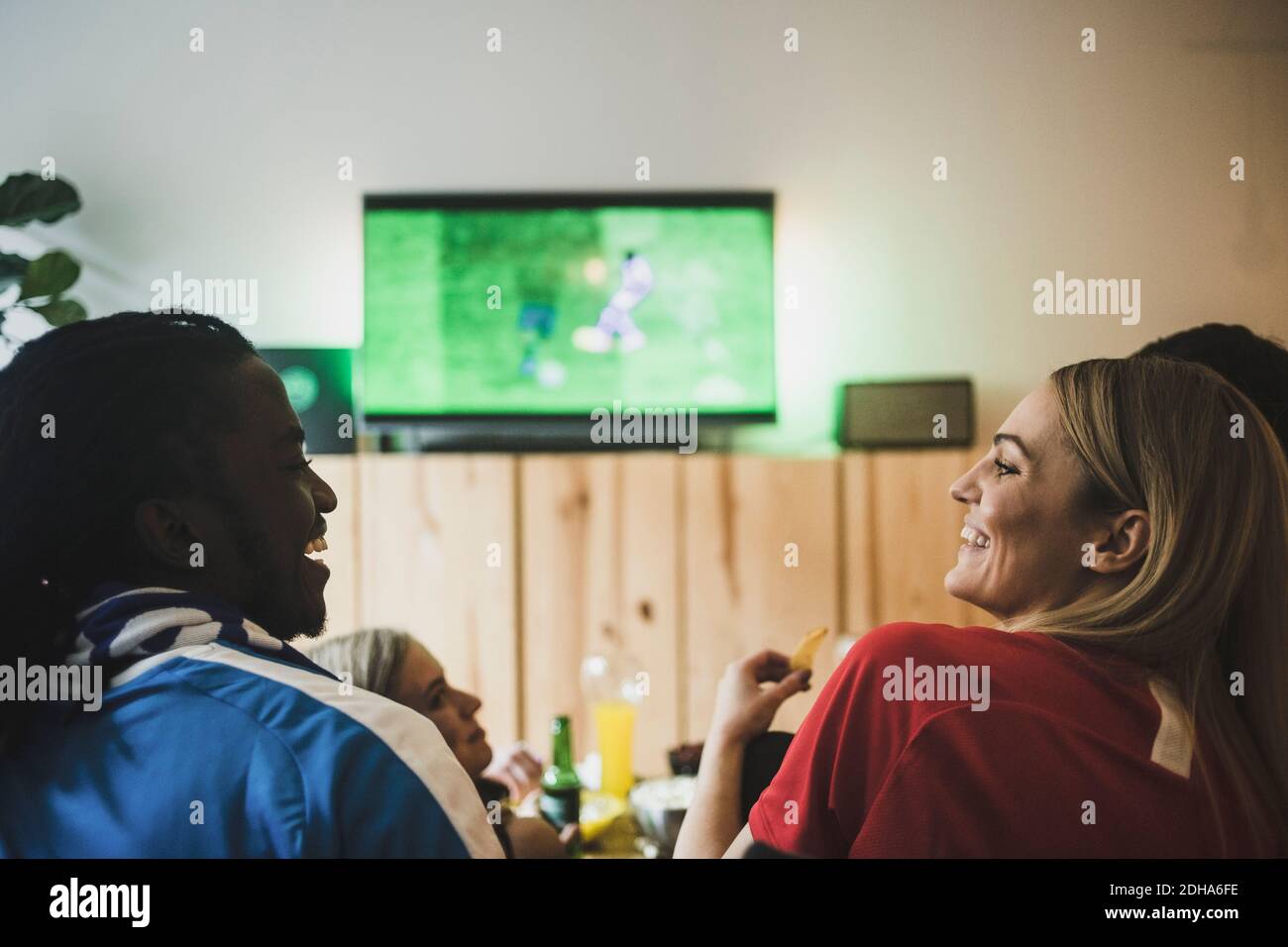 Sorridendo maschio e femmina guardando il calcio mentre si siede con gli amici a casa Foto Stock