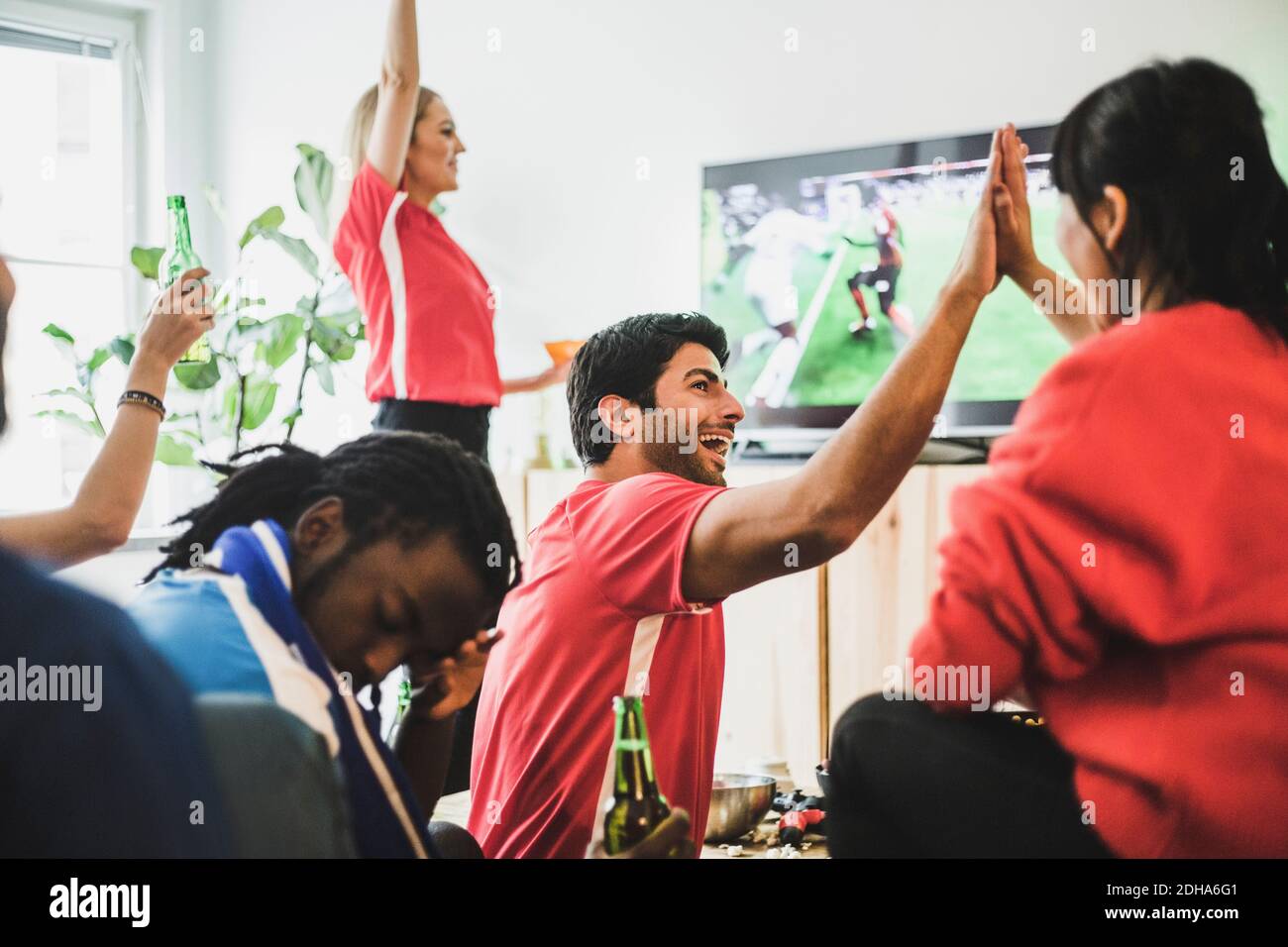 Giovane uomo seduto turbato mentre la squadra rossa festeggia la vittoria a. casa Foto Stock