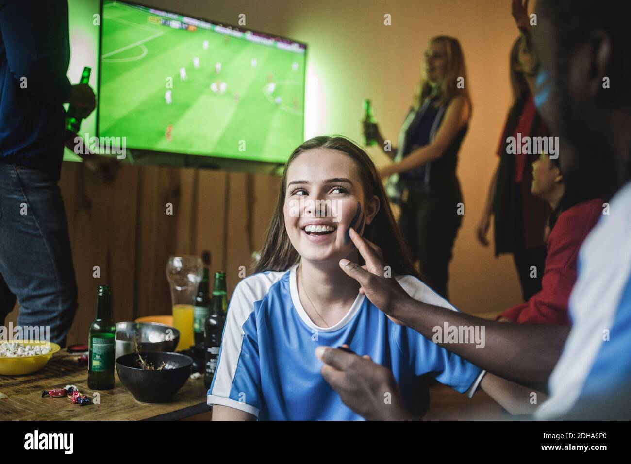 Uomo che applica la vernice di faccia sulla guancia della donna mentre guarda il calcio partita a casa Foto Stock