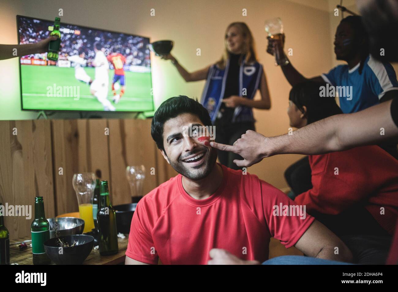 Mano tagliata dell'uomo che applica la vernice del viso sulla guancia dell'amico durante la partita di calcio Foto Stock
