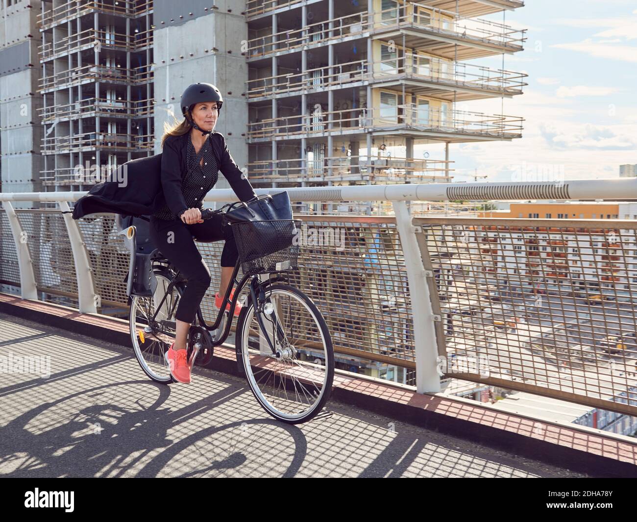 Donna matura in bicicletta sul ponte pedonale contro la costruzione Foto Stock