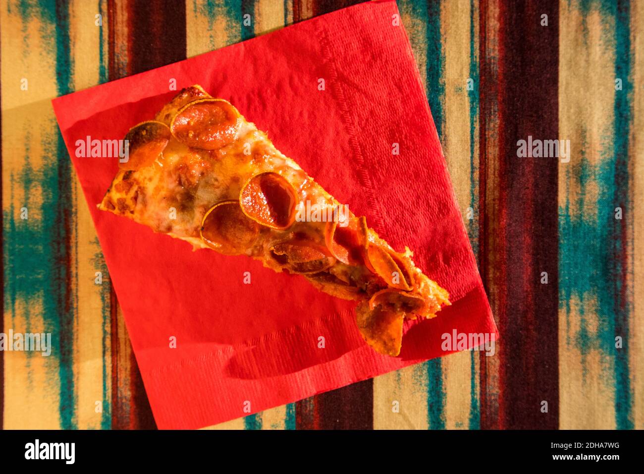 Una fetta di Pepperoni Pizza su un tovagliolo rosso un tavolo Foto Stock