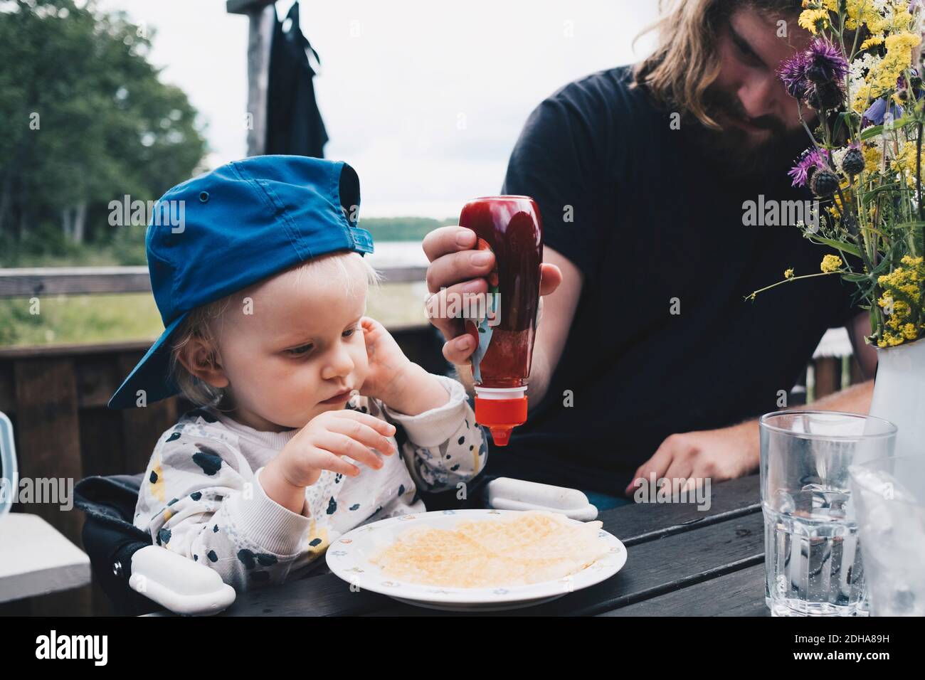 Ragazza che guarda il padre spremere il miele sui waffle a tavola Foto Stock