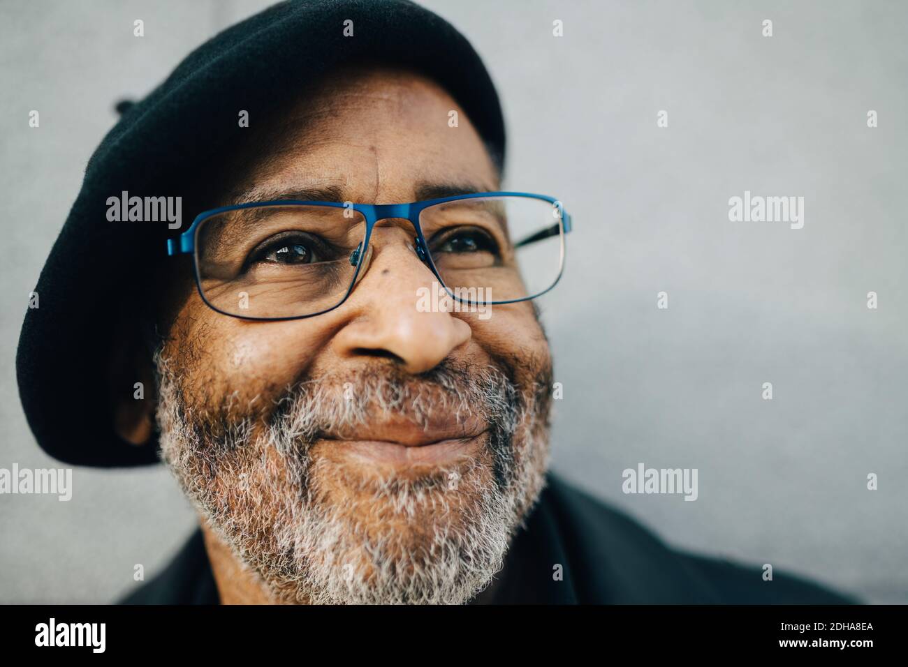 Uomo anziano con occhiali che guardano lontano contro il muro Foto Stock