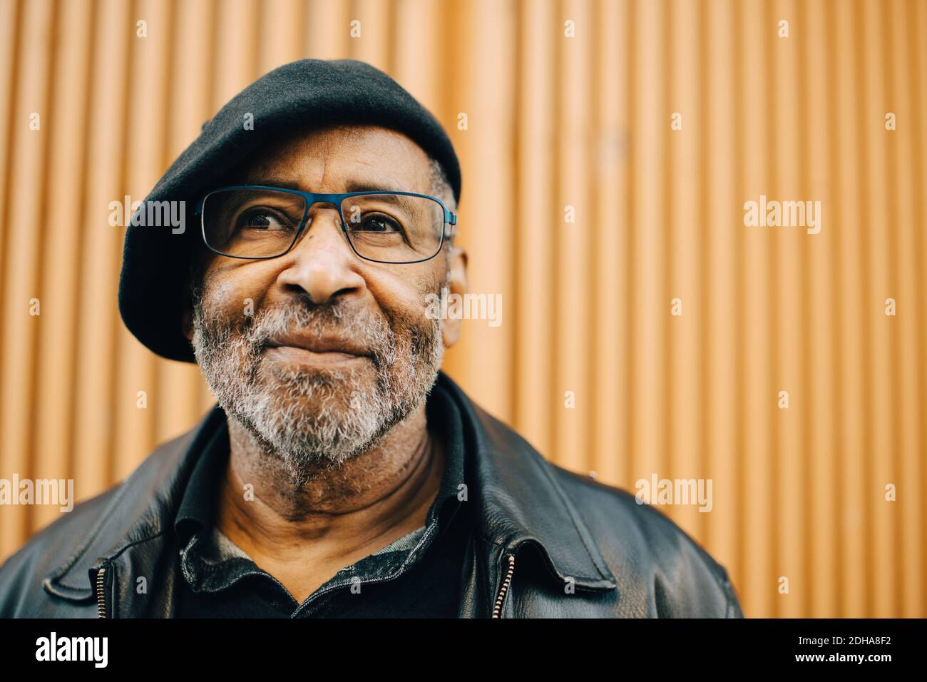 Uomo anziano sorridente con occhiali contro muro Foto Stock