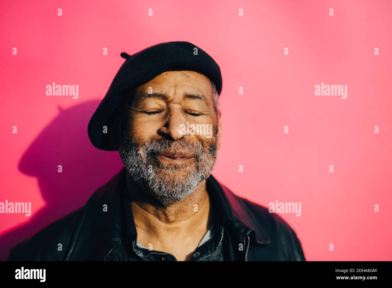Uomo anziano sorridente con occhi chiusi su sfondo rosa Foto Stock