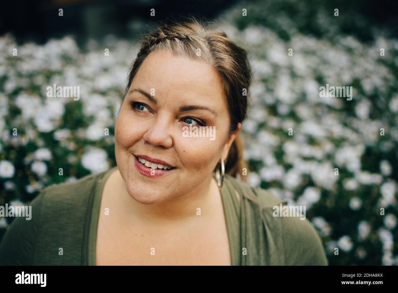 Donna matura sorridente che guarda via contro pianta fiorente Foto Stock