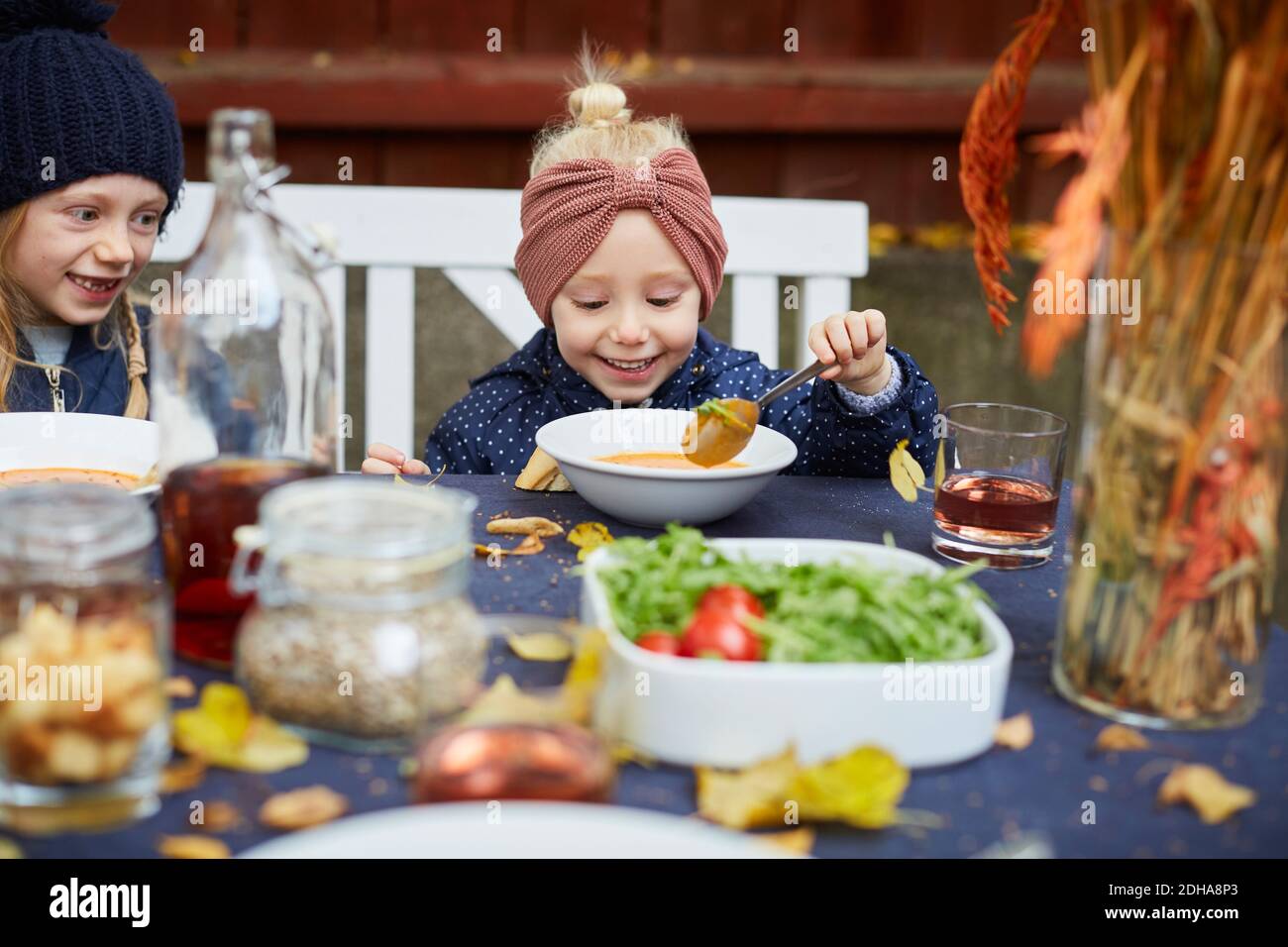 Sorridente ragazza che ha zuppa vegetariana mentre si siede dal fratello femmina a tavola Foto Stock