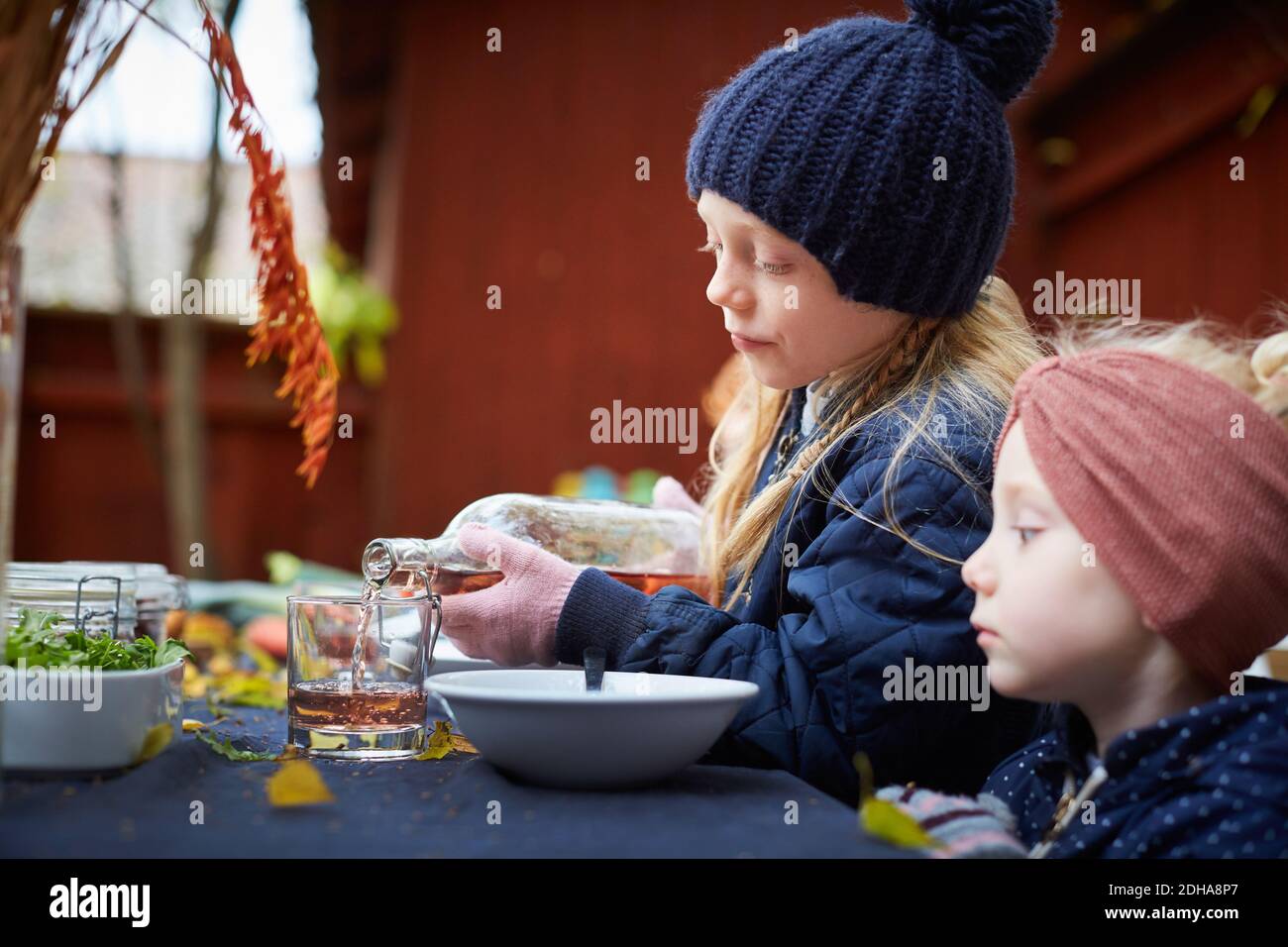 Ragazza che versa bere in vetro mentre si siede dal fratello femmina a tavola Foto Stock