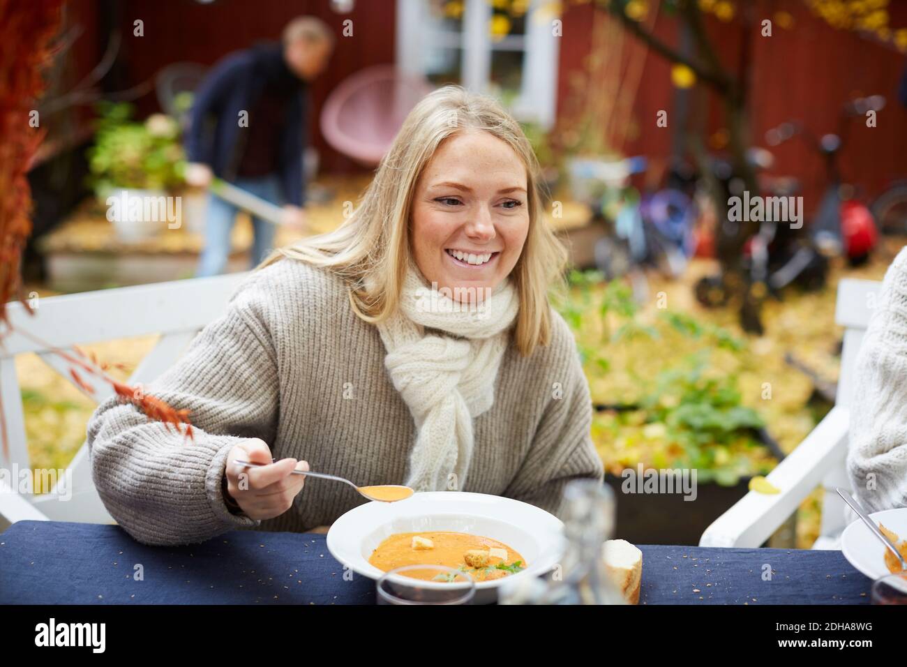 Donna felice con zuppa vegetariana seduto al tavolo in cortile Foto Stock