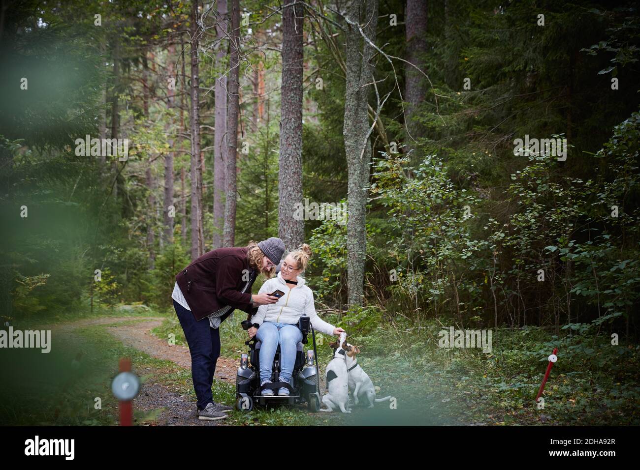 Uomo custode con donna disabile utilizzando il telefono cellulare in foresta Foto Stock