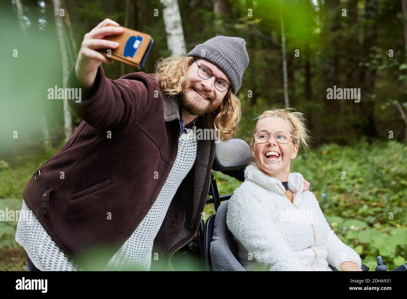 Giovane uomo di carriera che prende selfie con la donna disabile in foresta Foto Stock
