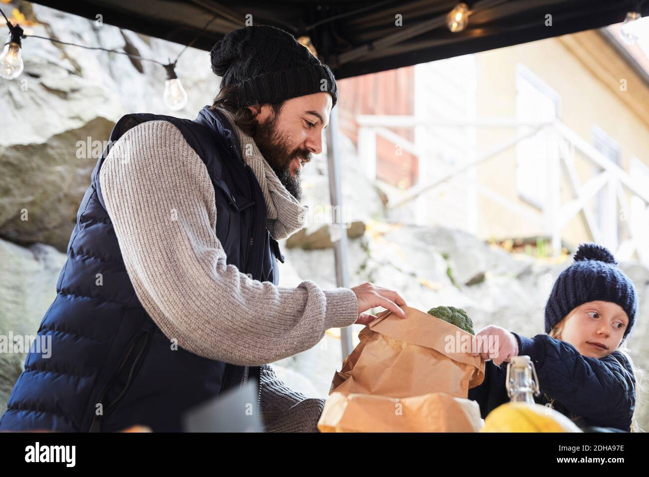 Ragazza che compra broccoli mentre il venditore maschio tiene il sacchetto di carta a. stallo del mercato Foto Stock