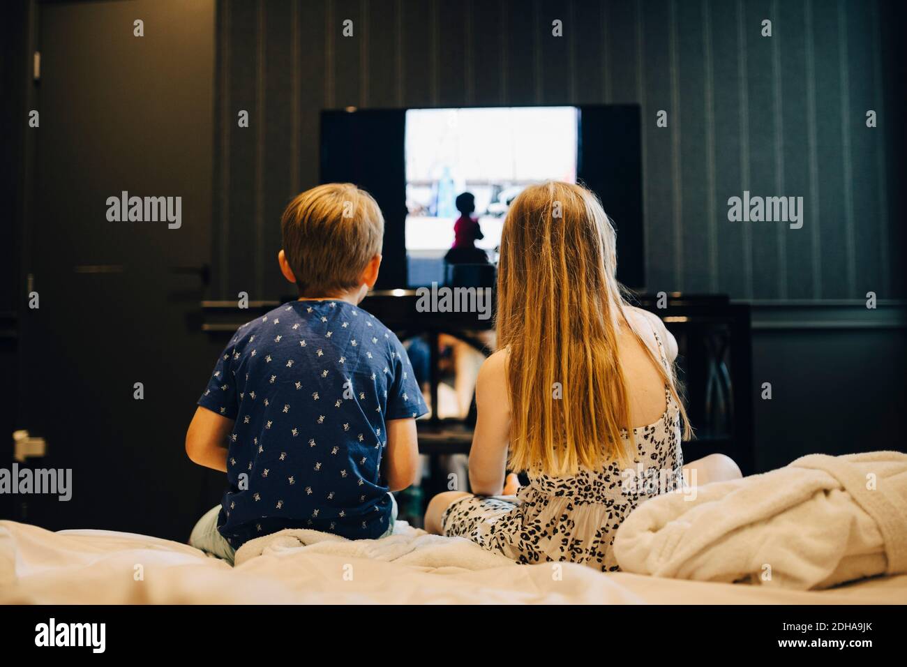 Vista posteriore dei fratelli che guardano la televisione mentre si siede a letto in camera d'albergo Foto Stock