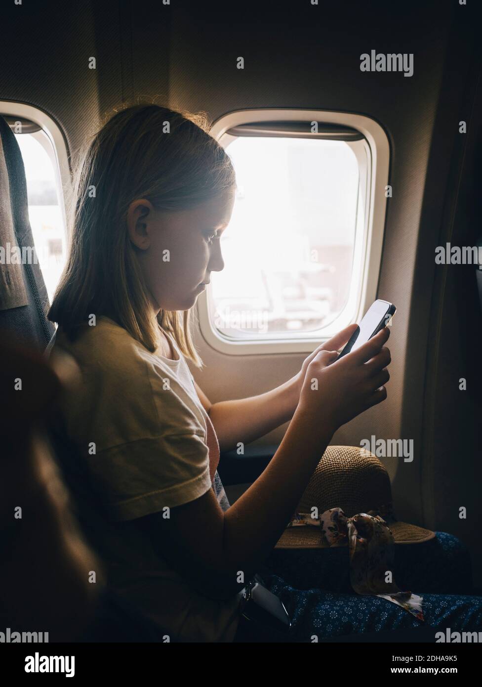 Vista laterale della ragazza che utilizza il telefono cellulare mentre si è seduti finestra dell'aereo Foto Stock