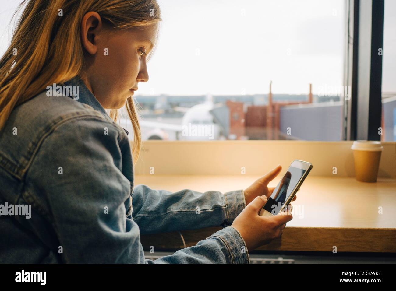 Vista laterale della ragazza che utilizza il telefono cellulare mentre si è seduti a. aeroporto Foto Stock