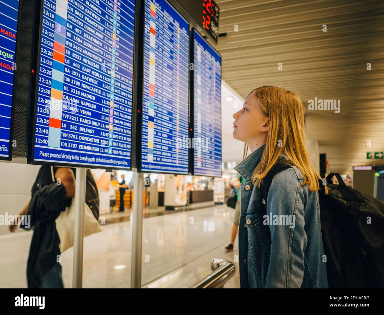 Vista laterale della ragazza che guarda la tavola di partenza mentre si è in piedi in aeroporto Foto Stock