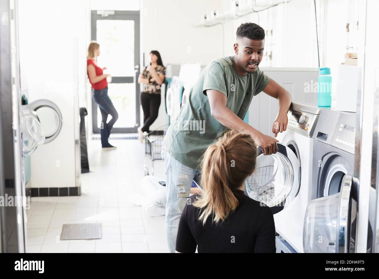 Studente universitario che parla con la donna lavando la macchina mentre gli amici in piedi sullo sfondo Foto Stock