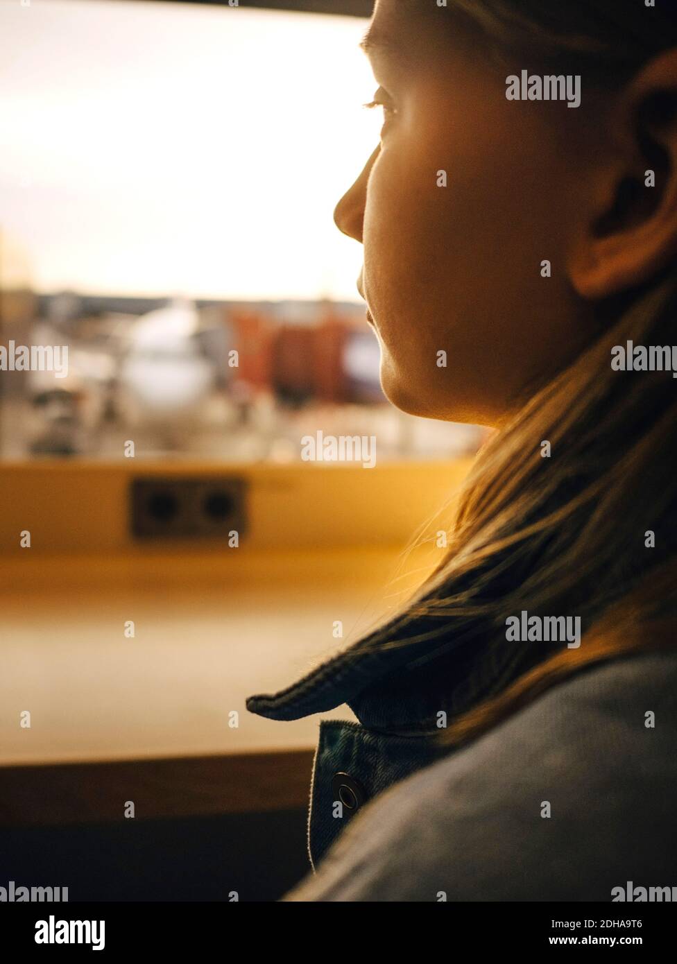 Ragazza che guarda attraverso la finestra mentre si siede all'aeroporto Foto Stock