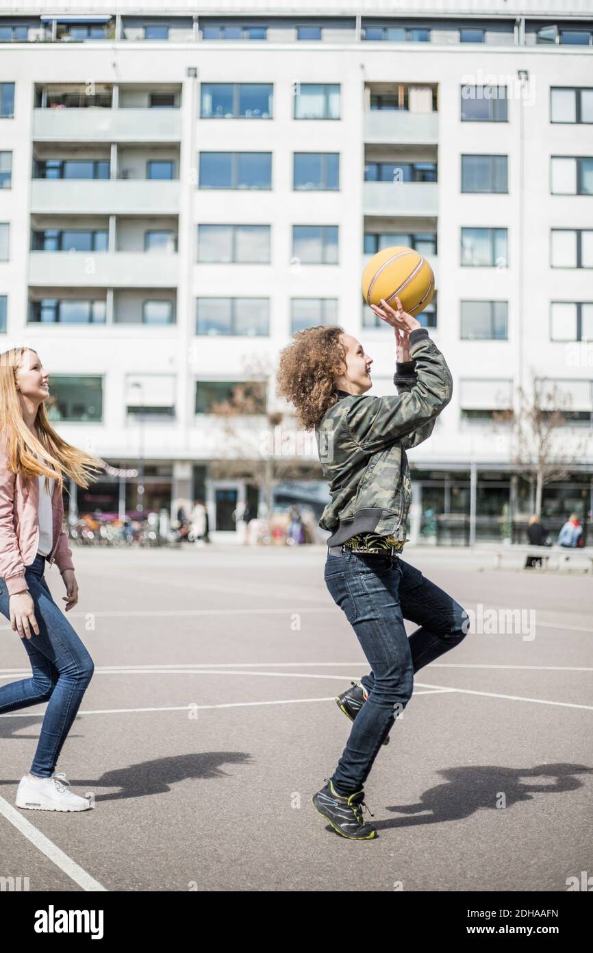 Vista laterale completa degli amici che giocano a basket contro l'edificio Foto Stock