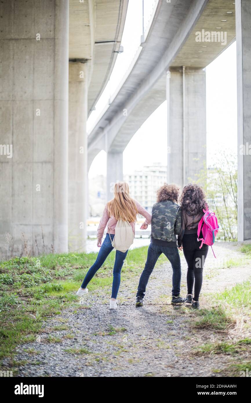 Giocosa ragazza che spinge gli amici mentre cammina sotto il ponte in città Foto Stock