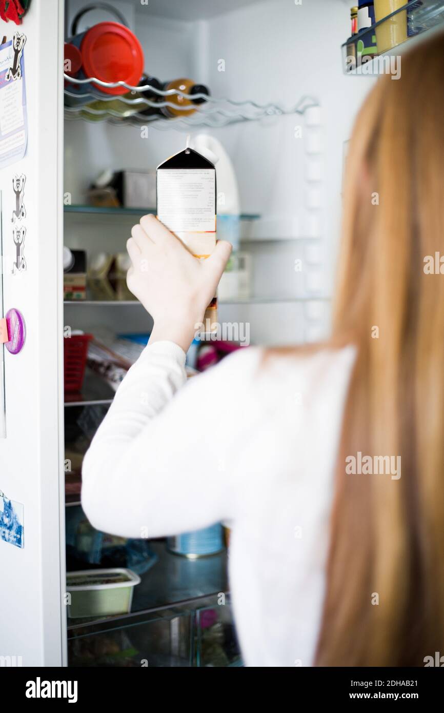 Vista posteriore della ragazza che tiene il cartone dal frigorifero a casa Foto Stock