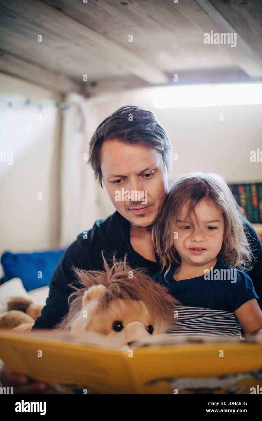 Padre leggere libro con la figlia mentre si siede in camera da letto Foto Stock