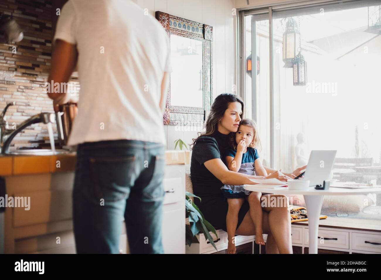 Madre che lavora su un computer portatile mentre figlia guarda il padre in piedi in cucina Foto Stock