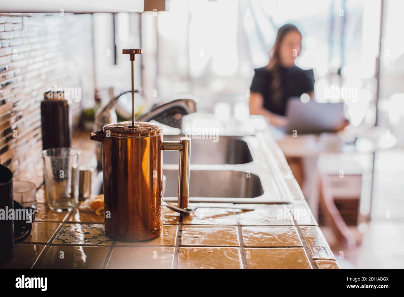 French press on wet kitchen counter mentre la donna lavora in sfondo Foto Stock