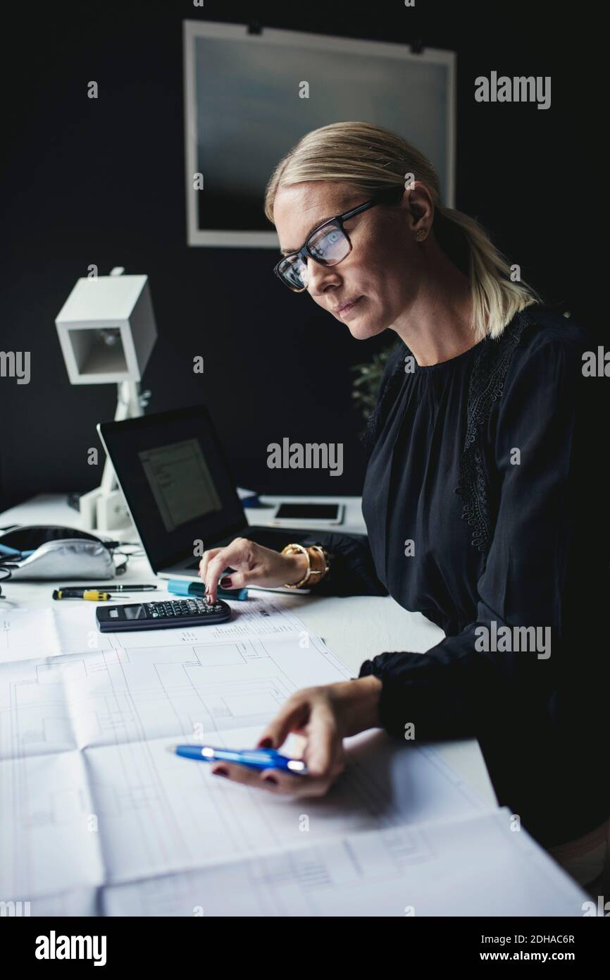 Donna d'affari che guarda il modello mentre usa la calcolatrice sulla scrivania Foto Stock