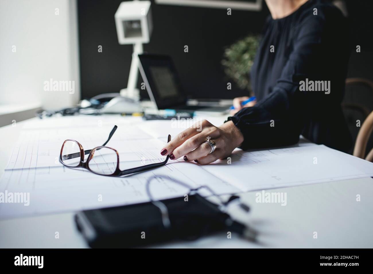 Sezione centrale dell'ingegnere femminile che tiene gli occhiali su BluePrint alla scrivania Foto Stock