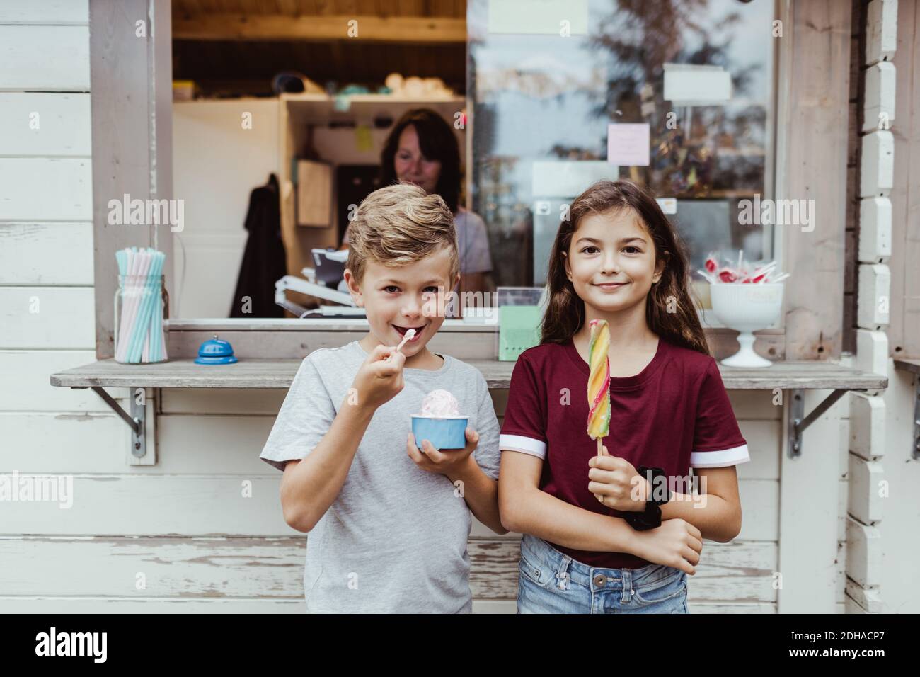 Ritratto del fratello che mangia cibo dolce mentre si è in piedi contro la concessione stand Foto Stock