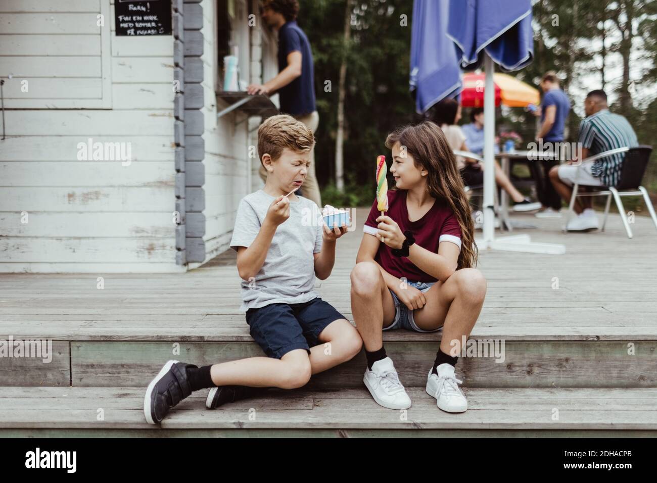 Tutta la lunghezza di fratello e sorella che mangia cibo dolce mentre seduto su scale di legno Foto Stock