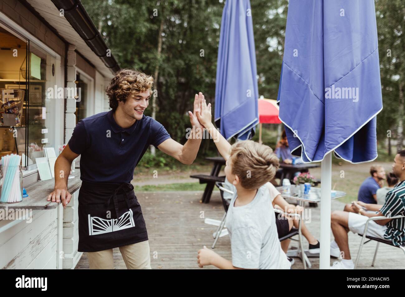 Sorridente giovane proprietario che dà high-five al cliente mentre sta vicino ristorante Foto Stock