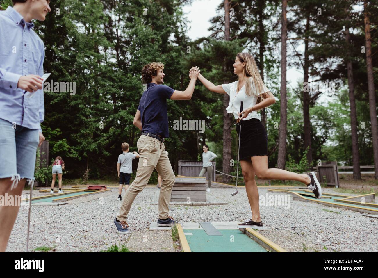 Tutta la lunghezza degli amici che danno high-five mentre gioca a golf in miniatura in cortile Foto Stock