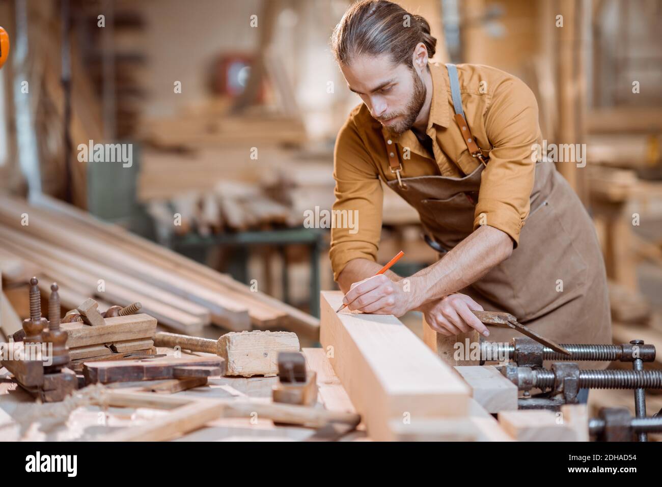 Bel falegname che lavora con un legno, segnando una tavola con una matita nel laboratorio di Falegnameria Foto Stock