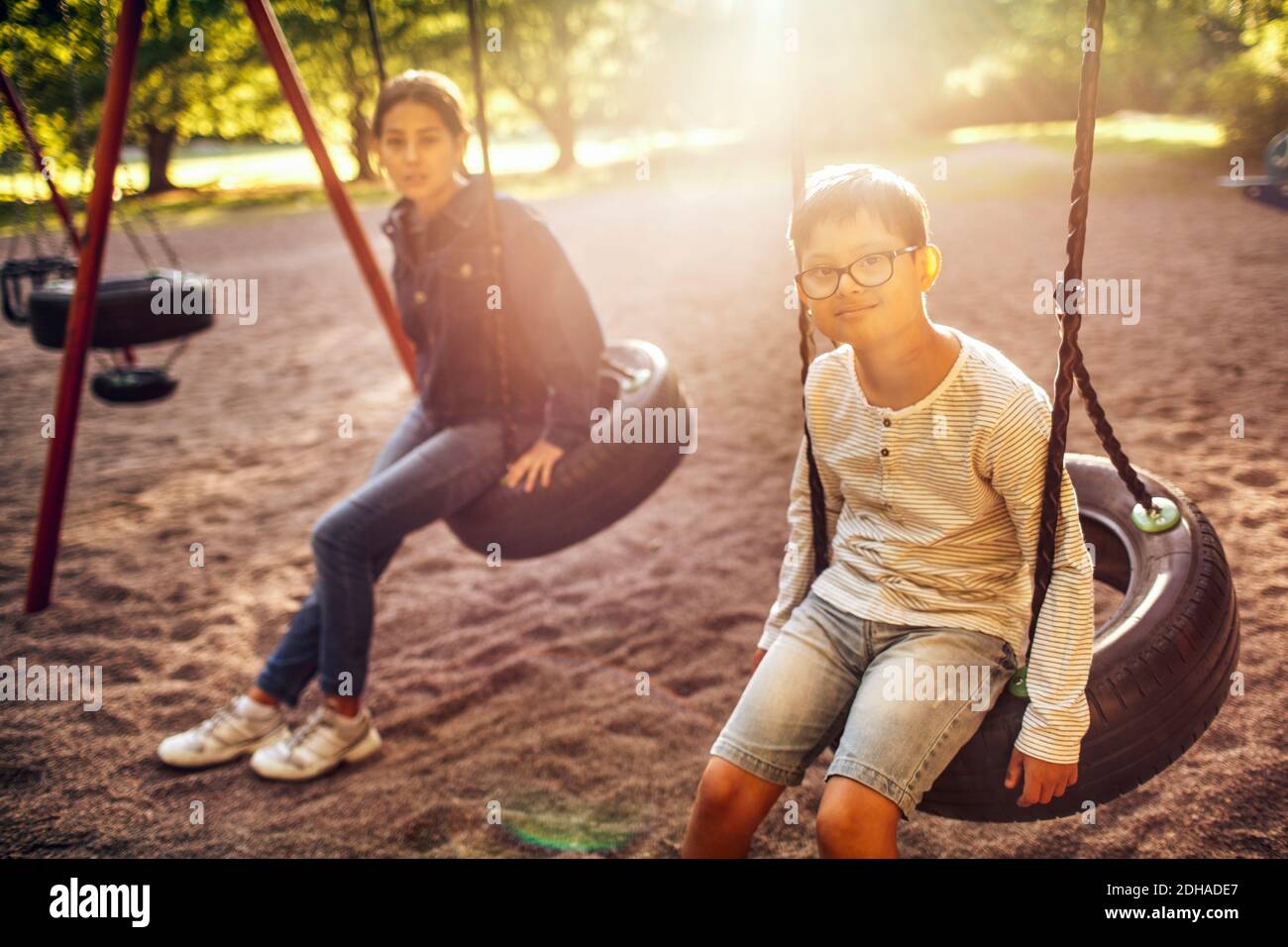 Ritratto di fratello e sorella seduti sull'altalena al parco durante il  giorno di sole Foto stock - Alamy
