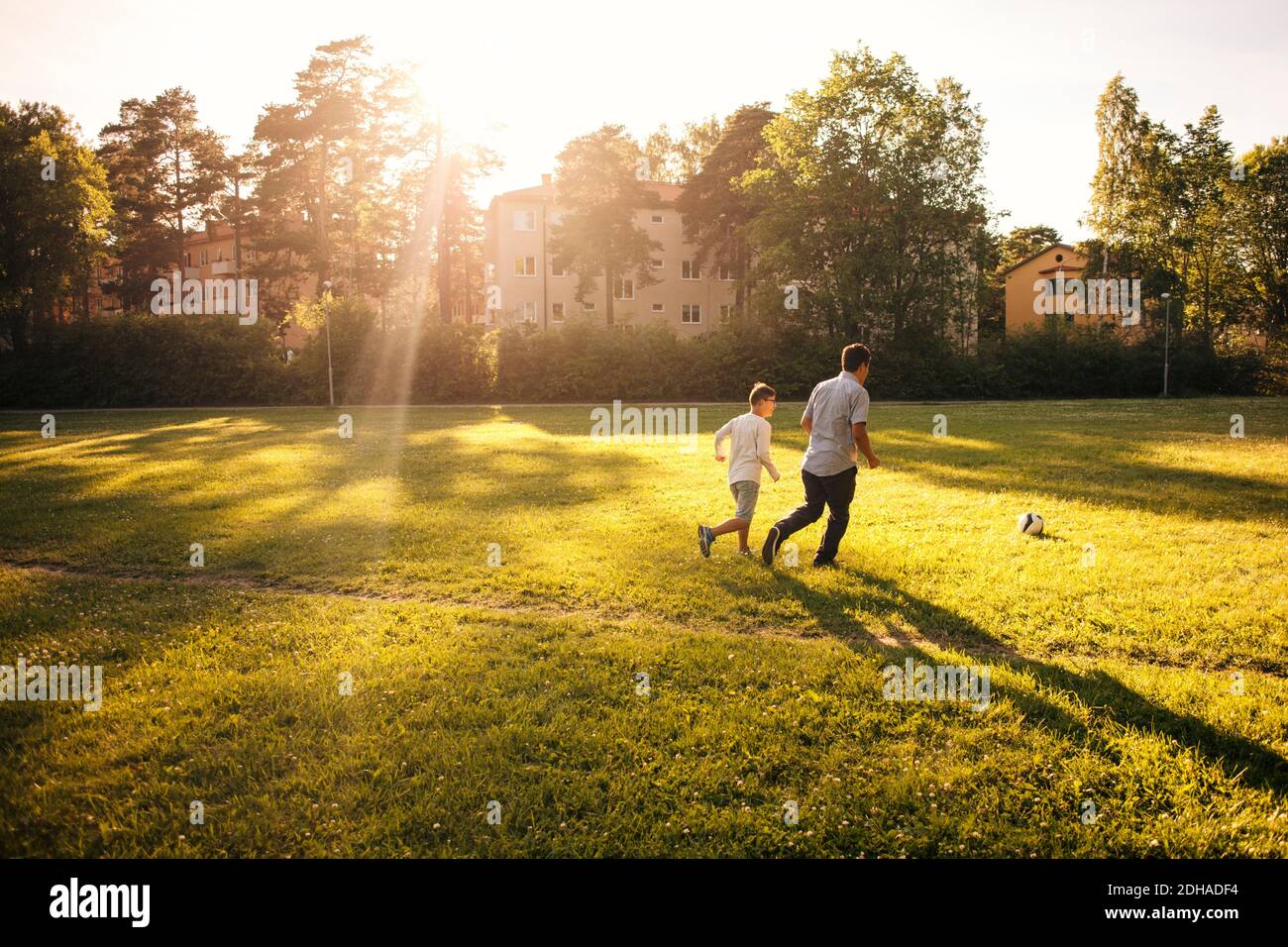 Tutta la lunghezza di padre e figlio che gioca a calcio sulla erba campo durante la giornata di sole Foto Stock