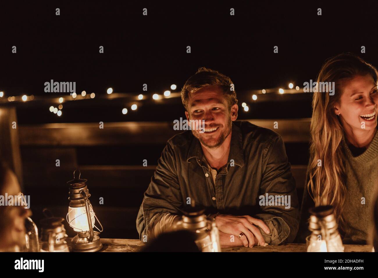 Uomo sorridente seduto con un'amica in ristorante di notte Foto Stock