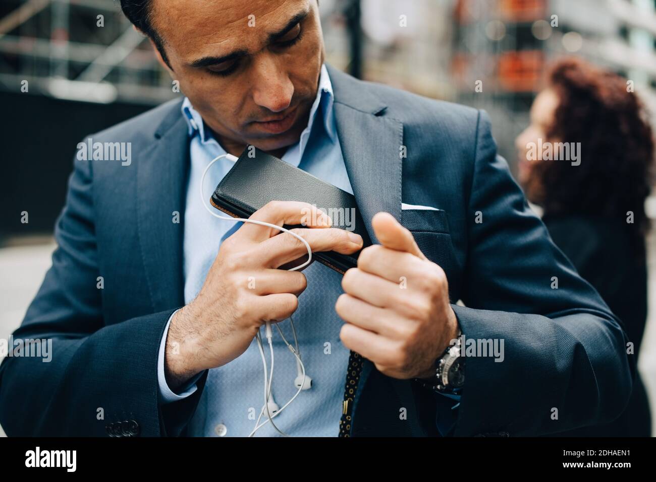Uomo d'affari maturo posizionamento telefono cellulare e cuffie intrauricolari in tuta tasca Foto Stock