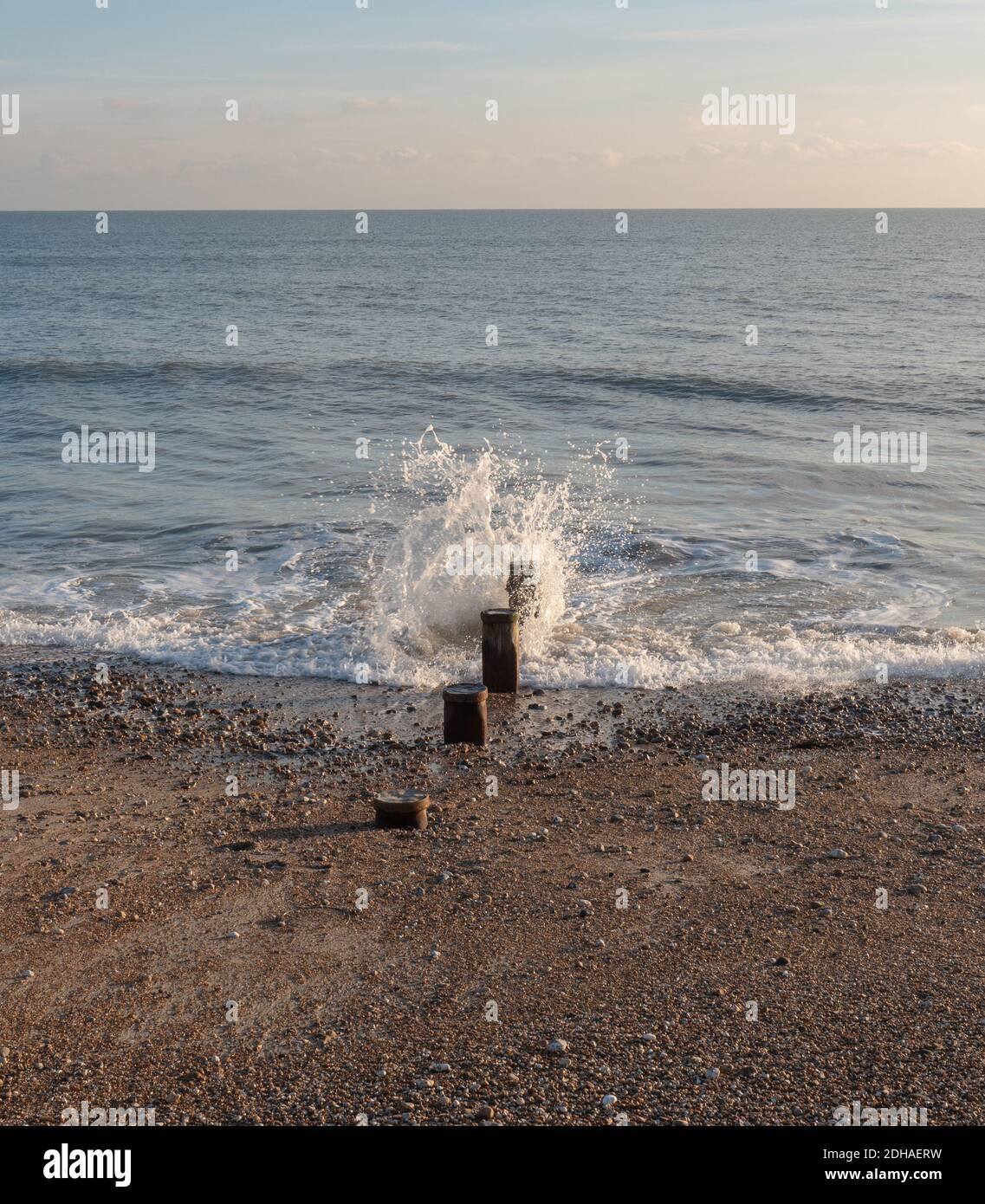 Le onde del mare si infrangono delicatamente contro i pali di legno sulla linea costiera. Foto Stock