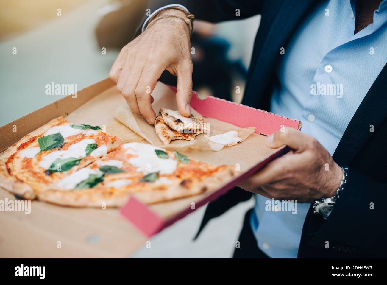 Mezza sezione di uomo d'affari che mangia pizza da scatola di cartone in città Foto Stock