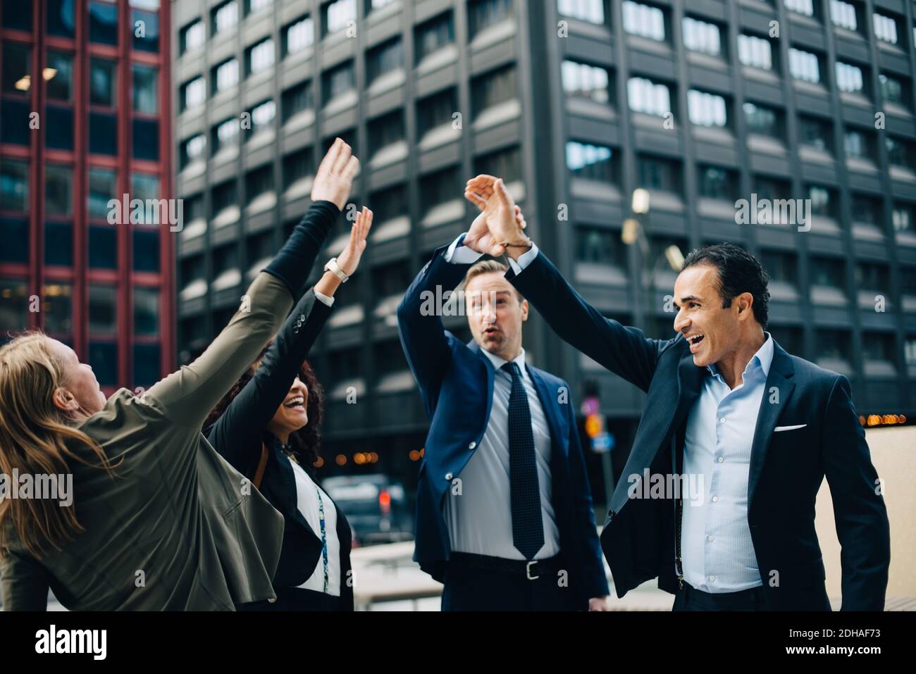 Sorridente business multietnico in piedi con le mani sollevate contro l'edificio in città Foto Stock