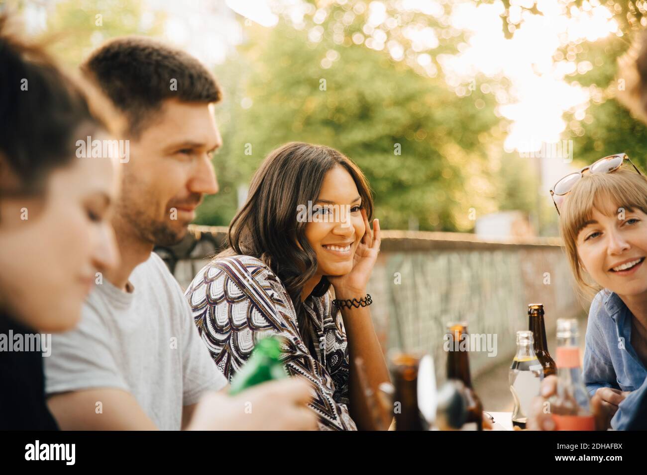 Giovane donna sorridente mentre si siede con gli amici alla riunione sociale Foto Stock