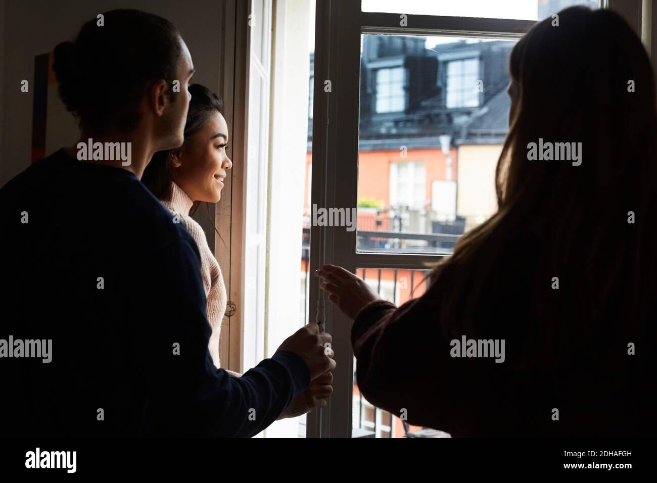 Sorridendo gli amici guardando attraverso la finestra mentre si trova in appartamento in affitto Foto Stock