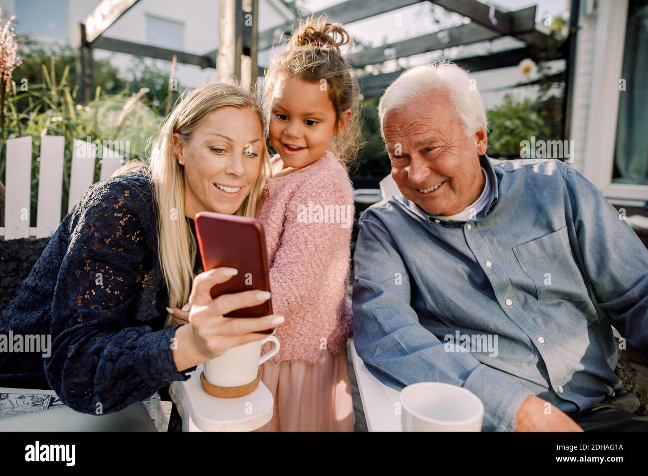 Sorridendo nonno e nipote prendendo selfie con il telefono cellulare mentre seduto in cortile Foto Stock