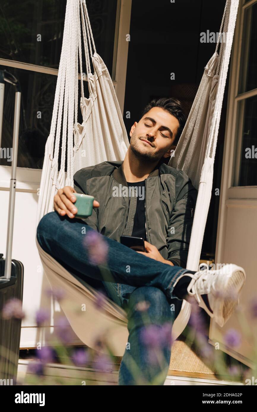 Tutta la lunghezza del giovane uomo che si rilassa mentre si siede in swing contro la porta Foto Stock