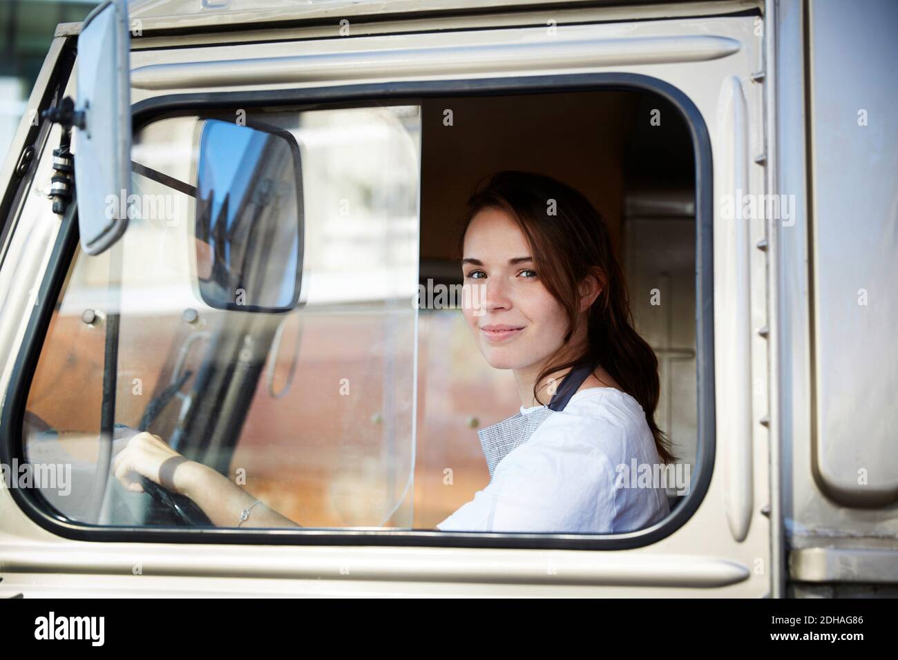 Ritratto di giovane donna sorridente proprietario guida camion di cibo dentro città Foto Stock