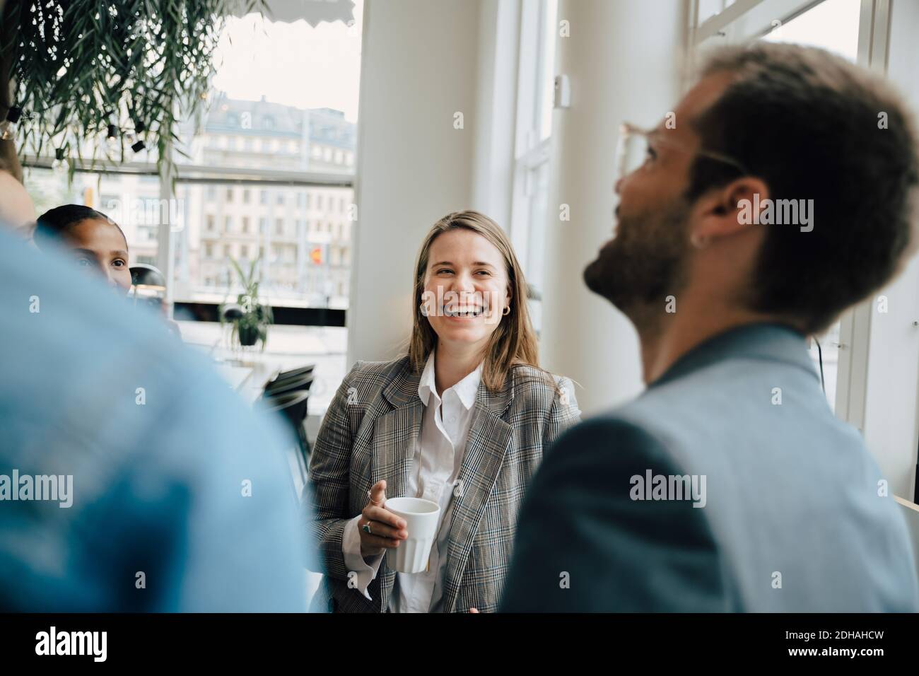 Donna d'affari sorridente che ha caffè con i colleghi in un luogo di lavoro creativo Foto Stock